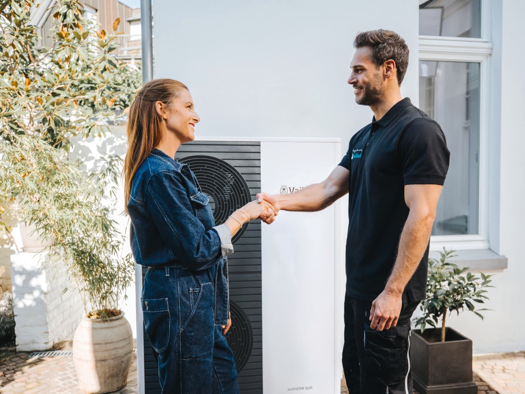 Ein Installateur, der einer Frau vor einer Wärmepumpe die Hand schüttelt