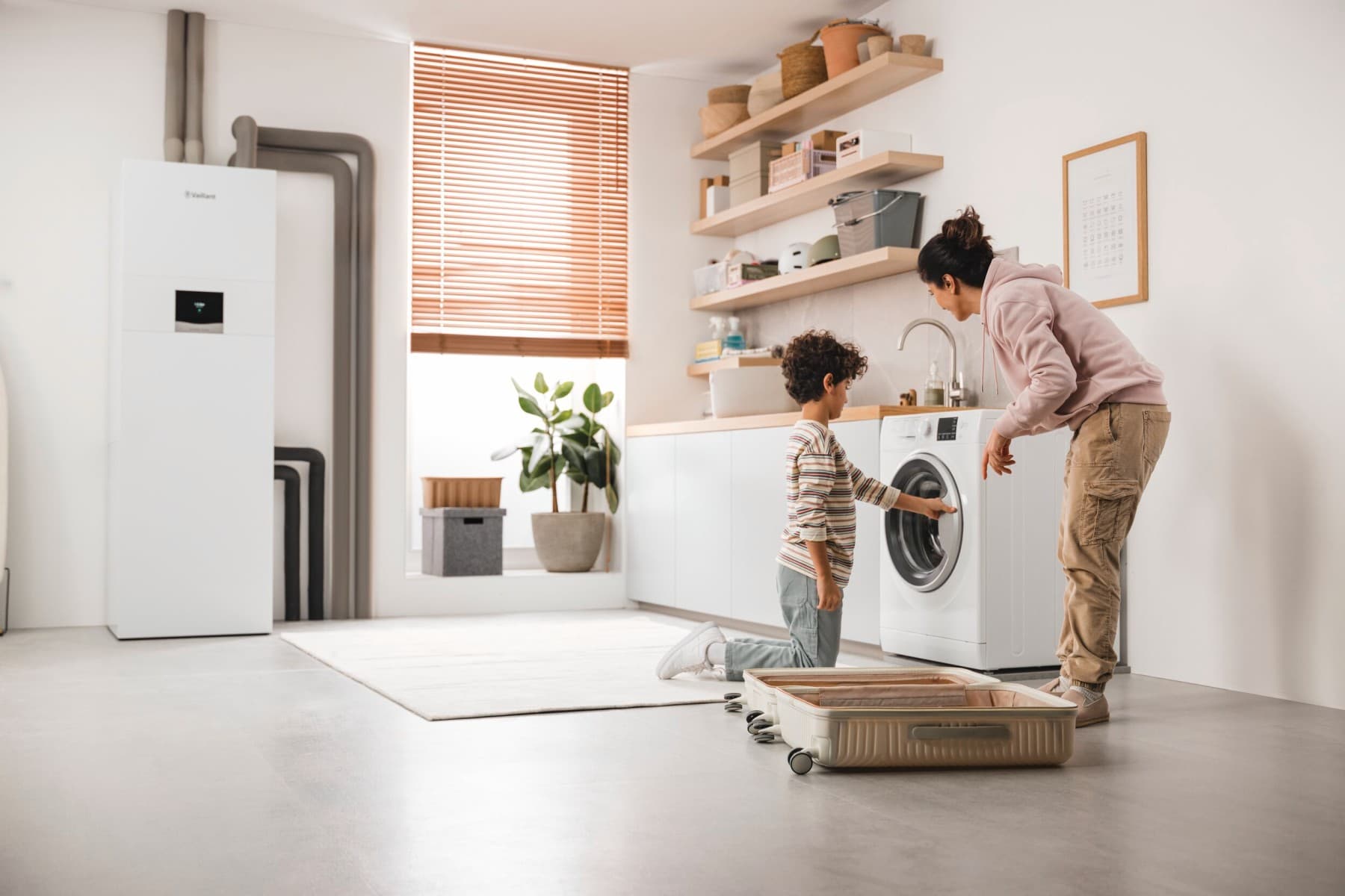 Mutter und Sohn überprüfen die Waschmaschine; im Hintergrund ist eine Erdwärmepumpe zu sehen.