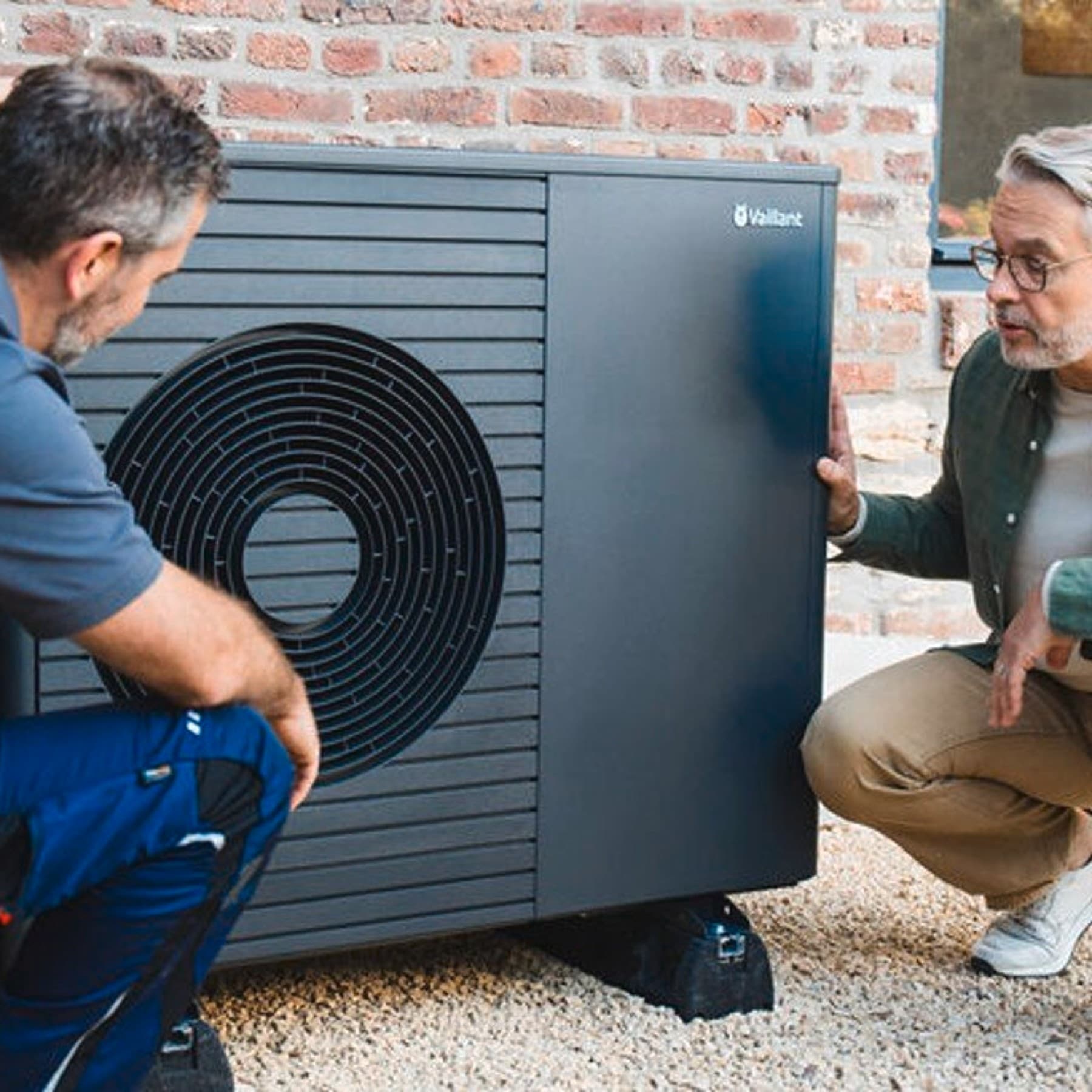 Servicetechniker arbeitet an einer Wärmepumpe vor einem Mann